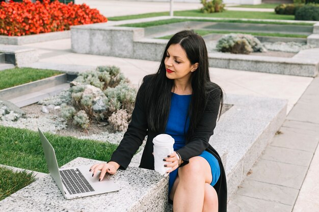 Femme d&#39;affaires avec une tasse de récupération travaillant sur un ordinateur portable