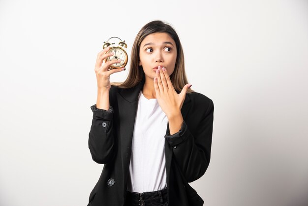 Femme d'affaires tenant un réveil sur un mur blanc.