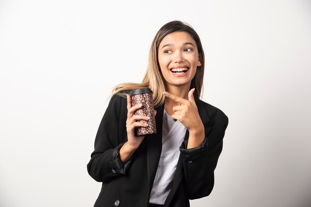 Femme d'affaires tenant la tasse et posant sur le mur blanc.