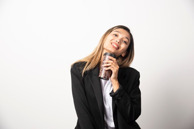 Femme d'affaires tenant la tasse et posant sur le mur blanc.