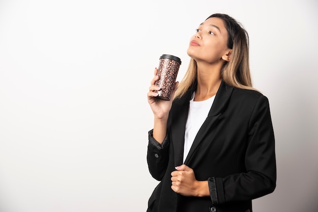 Femme d'affaires tenant la tasse et posant sur le mur blanc.