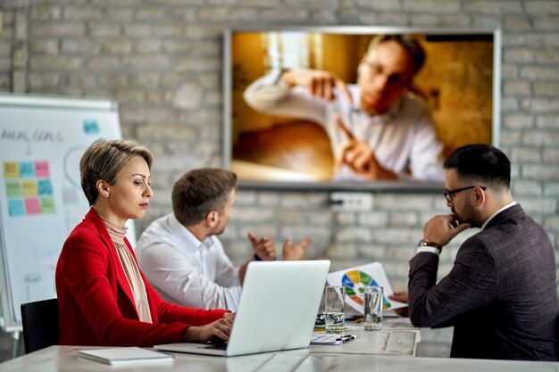 Femme d'affaires travaillant sur un ordinateur lors d'une réunion au bureau Un de ses collègues rejoint la réunion par appel vidéo