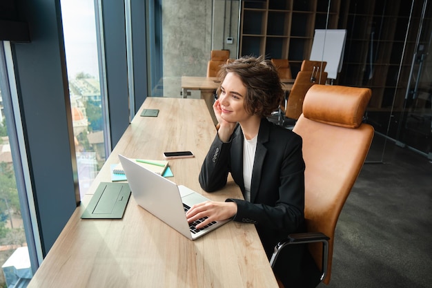 Femme d'affaires travaillant sur un ordinateur portable assise au bureau en costume attendant que le client prépare la documentation