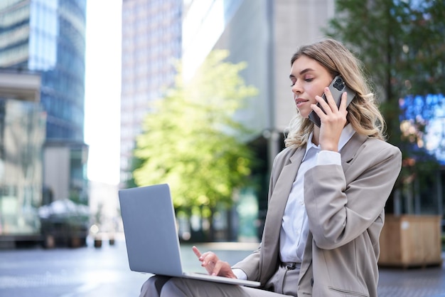 Photo gratuite femme d'affaires vérifiant le schéma et travaillant sur un ordinateur portable appelant quelqu'un sur un téléphone portable assis à l'extérieur je