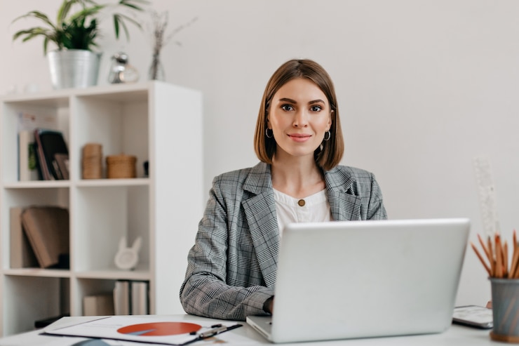 Photo gratuit femme d'affaires en veste à carreaux avec sourire alors qu'il était assis au bureau dans son bureau.