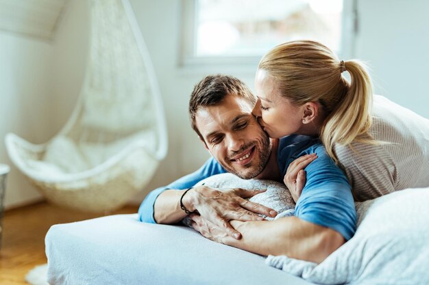 Femme affectueuse embrassant son petit ami en position couchée dans son lit.