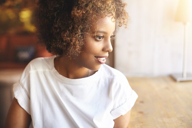 Femme africaine en chemise à la mode blanche en attente d'amis pour la rejoindre au café confortable.