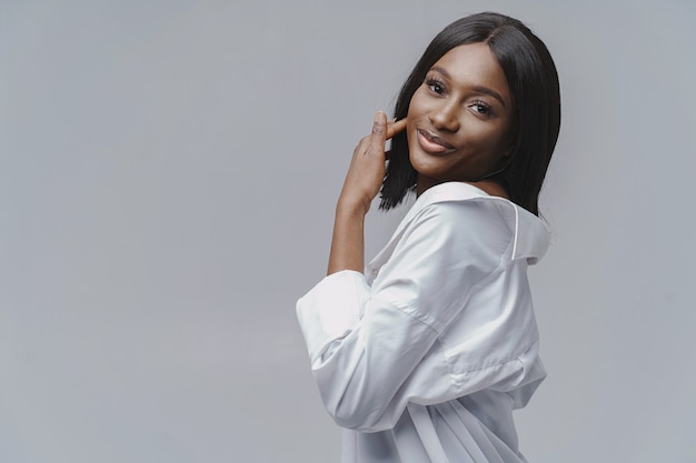 Femme africaine dans un studio. Mur blanc. Femme en chemise blanche.