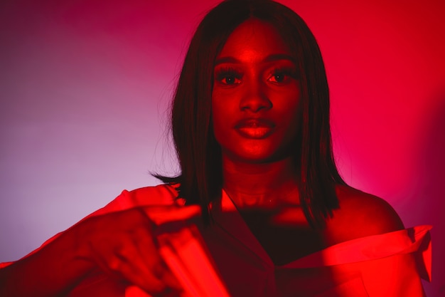 Femme africaine dans un studio. Mur rouge. Femme en chemise blanche.