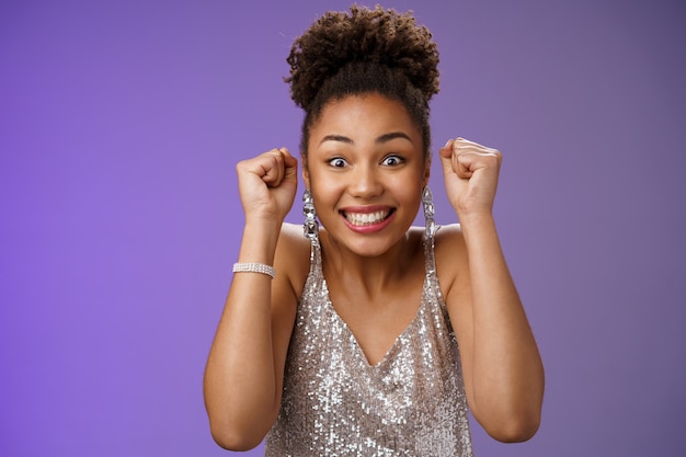 Photo gratuite femme africaine excitée dans une élégante robe argentée brillante souriante ravie de gagner le poing levé...