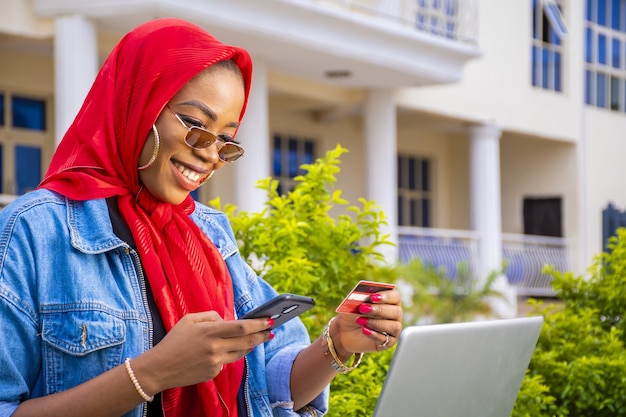 Photo gratuite femme africaine, faire du shopping en ligne à l'aide d'un ordinateur portable et d'un smartphone tout en tenant sa carte de crédit