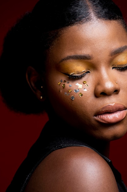 Femme africaine en gilet de cuir avec des confettis brillants sur ses joues