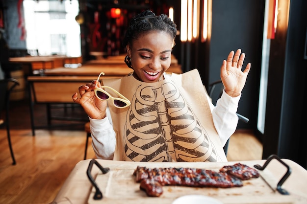 Photo gratuite une femme africaine mange des côtes levées grillées chaudes et épicées sur un bureau en bois