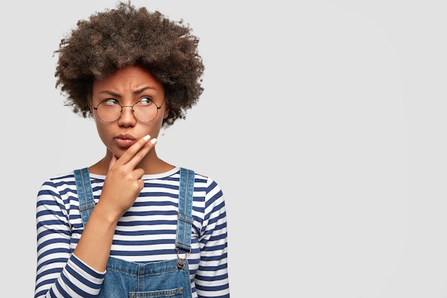 Photo gratuite femme africaine à la peau sombre pensive tient le menton et regarde pensivement de côté