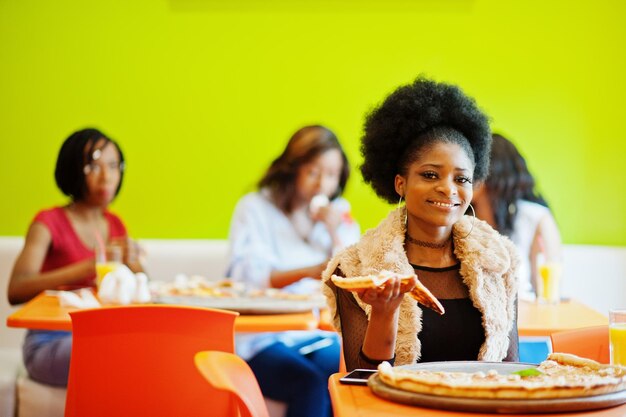 Femme africaine avec pizza assis au restaurant contre des filles à la peau foncée