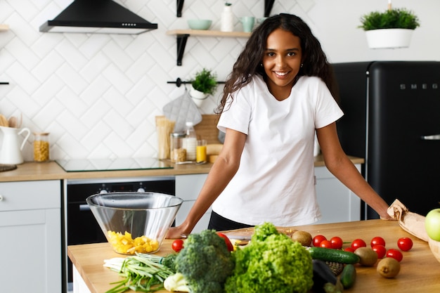 Femme africaine se tient devant un bureau de cuisine avec différents fruits et légumes