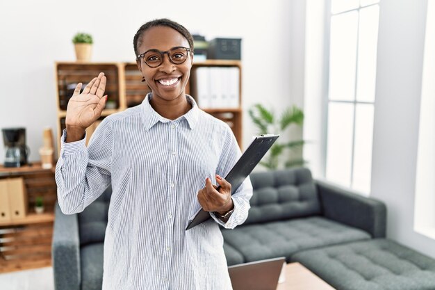 Femme africaine travaillant à la clinique de psychologie renonçant à dire bonjour heureux et souriant, geste de bienvenue amical