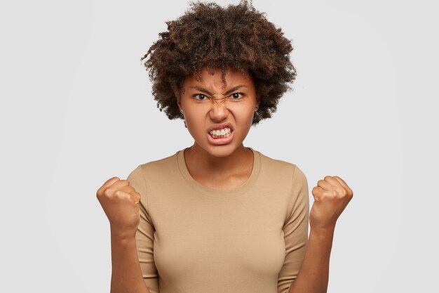 Une femme afro-américaine agacée serre les dents et les poings, étant maussade