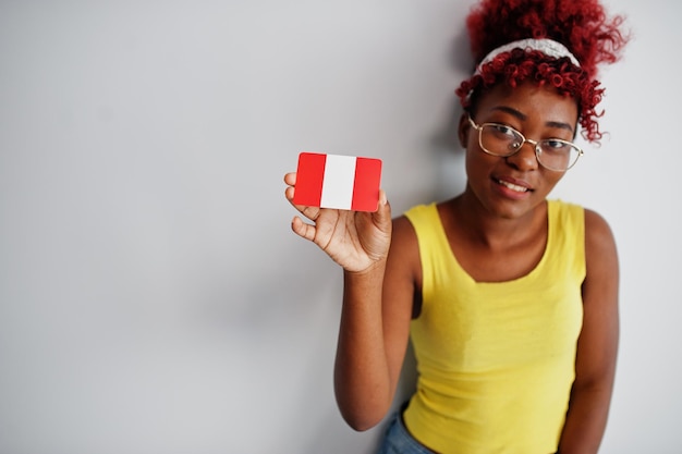 Une femme afro-américaine aux cheveux afro porte un singulet jaune et des lunettes tient le drapeau du Pérou isolé sur fond blanc