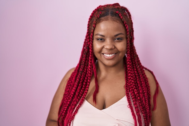 Femme afro-américaine aux cheveux tressés debout sur fond rose les mains jointes et les doigts croisés souriant détendu et joyeux. succès et optimiste