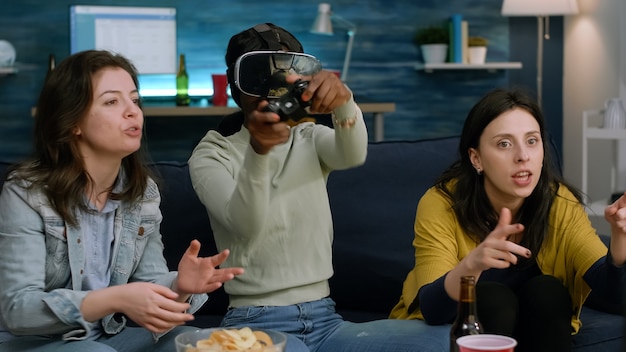 Femme afro-américaine bouleversée portant un casque de réalité virtuelle perdant des jeux vidéo en ligne à l'aide d'un contrôleur ...