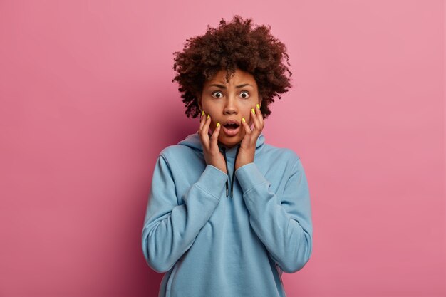 Une femme afro-américaine choquée et effrayée regarde avec les yeux grands ouverts