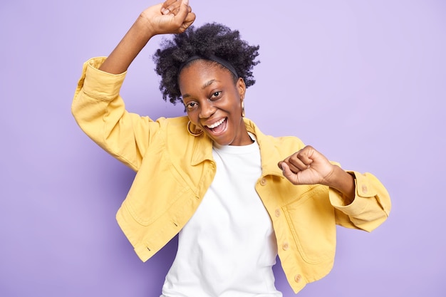 Une femme afro-américaine détendue et heureuse danse et s'amuse à lever les mains sans soucis, elle aime la musique