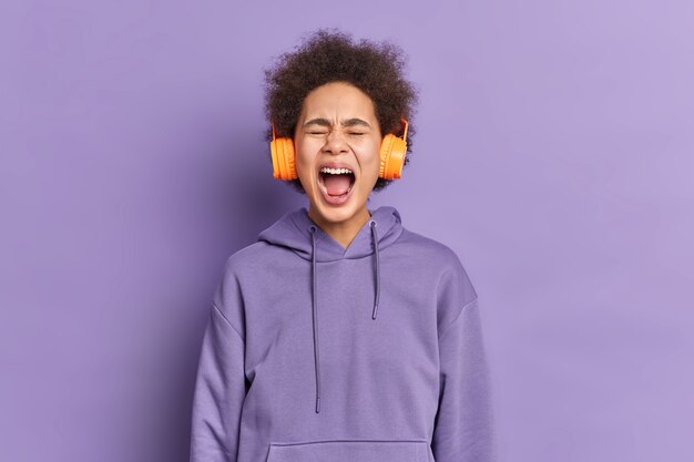 Une femme afro-américaine émotionnelle crie fort et garde la bouche ouverte vêtue d'un sweat à capuche.