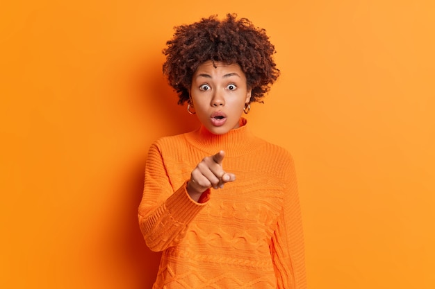 Une femme afro-américaine émotive aux cheveux bouclés regarde les yeux écarquillés indique directement à la caméra retient son souffle voit une offre inattendue