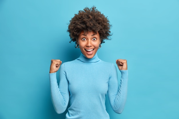 Photo gratuite une femme afro-américaine excitée qui réussit serre les poings célèbre son succès dans sa carrière dit oui sourit largement