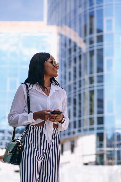 Femme afro-américaine à l&#39;extérieur par le gratte-ciel avec téléphone