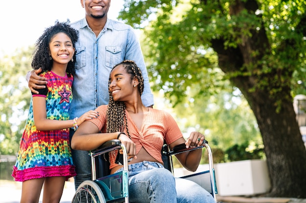 Une femme afro-américaine en fauteuil roulant profitant d'une promenade à l'extérieur avec sa fille et son mari.