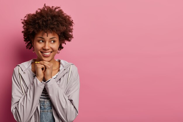 Femme afro-américaine garde les mains sous le menton, voit la belle vue de côté