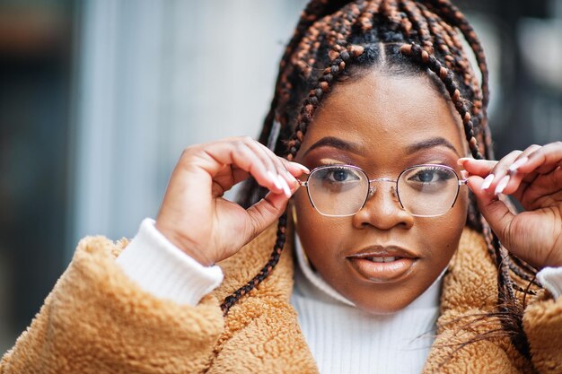 Une femme afro-américaine glamour dans des lunettes de manteau de fourrure chaude pose dans la rue