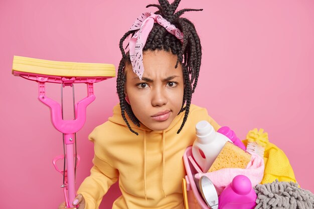 Une femme afro-américaine insatisfaite a des poses de dreadlocks avec des produits de nettoyage