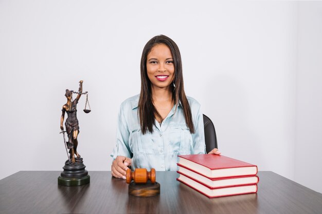 Femme afro-américaine joyeuse à table avec marteau, livres et statue