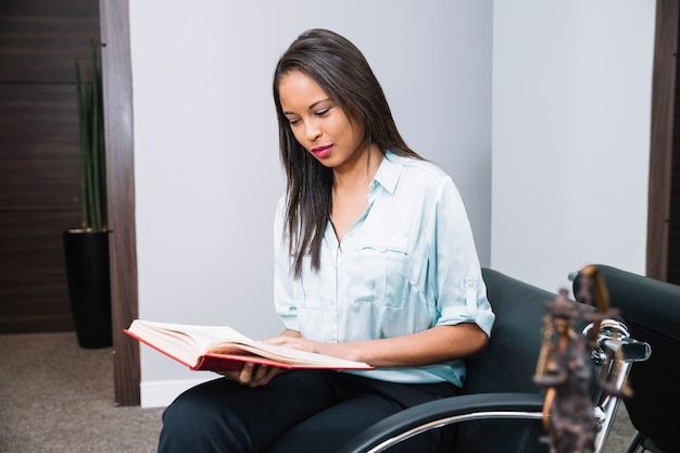 Photo gratuite femme afro-américaine avec livre assis sur un fauteuil de bureau