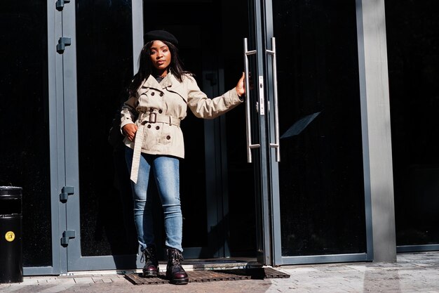 Une femme afro-américaine à la mode porte un béret et un manteau debout contre la porte