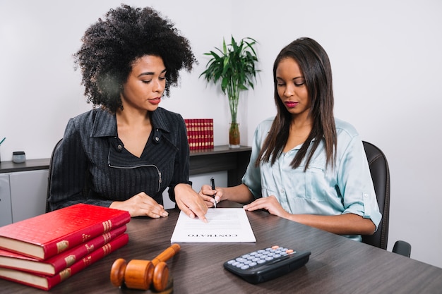 Femme afro-américaine pointant sur un document près de Dame avec un stylo à la table