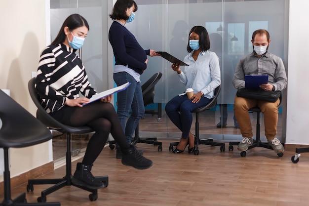 Femme afro-américaine recevant une offre d'emploi du directeur du service financier enceinte dans la salle d'attente. Divers candidats dans le hall lisant le règlement intérieur de l'entreprise.