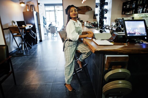 Femme afro-américaine en salopette et béret assis au comptoir du bar