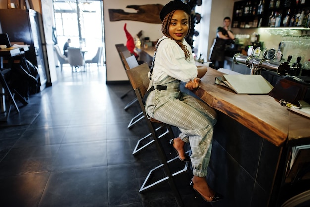 Photo gratuite femme afro-américaine en salopette et béret assis au comptoir du bar