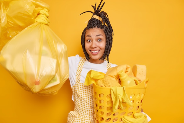 Une femme afro-américaine souriante avec des dreadlocks aime les travaux ménagers tient un sac en polyéthylène