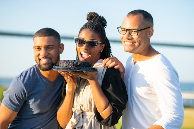 Femme afro-américaine souriante tenant un gâteau au chocolat. Heureux jeunes posant ensemble. Fête d'anniversaire