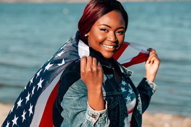 Femme afro-américaine tenant le drapeau américain derrière le dos