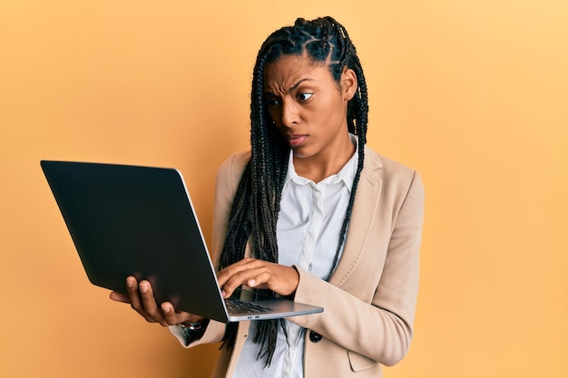 Femme afro-américaine travaillant à l'aide d'un ordinateur portable sceptique et nerveux, fronçant les sourcils contrarié à cause d'un problème. personne négative.