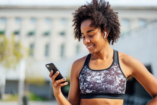 Femme afro athlétique à l'aide de son téléphone portable et se détendre après un entraînement à l'extérieur