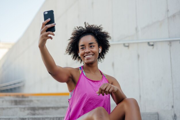Femme afro athlétique prenant un selfie avec son téléphone portable et se détendre après un entraînement à l'extérieur