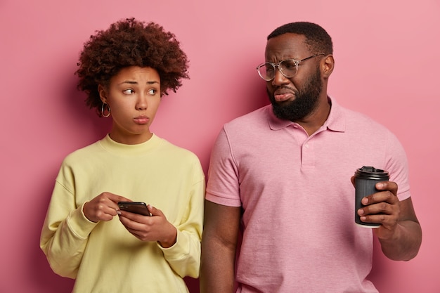 Femme afro malheureuse montre quelque chose dans le smartphone avec une expression triste