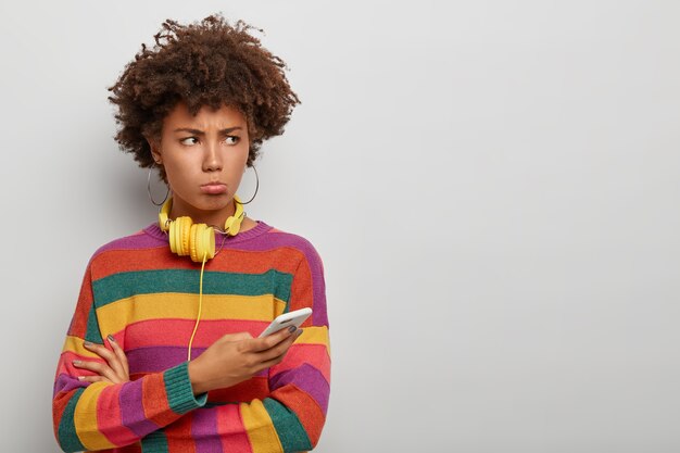 Femme afro millénaire insatisfaite regarde avec une expression offensée malheureuse de côté, utilise un téléphone mobile